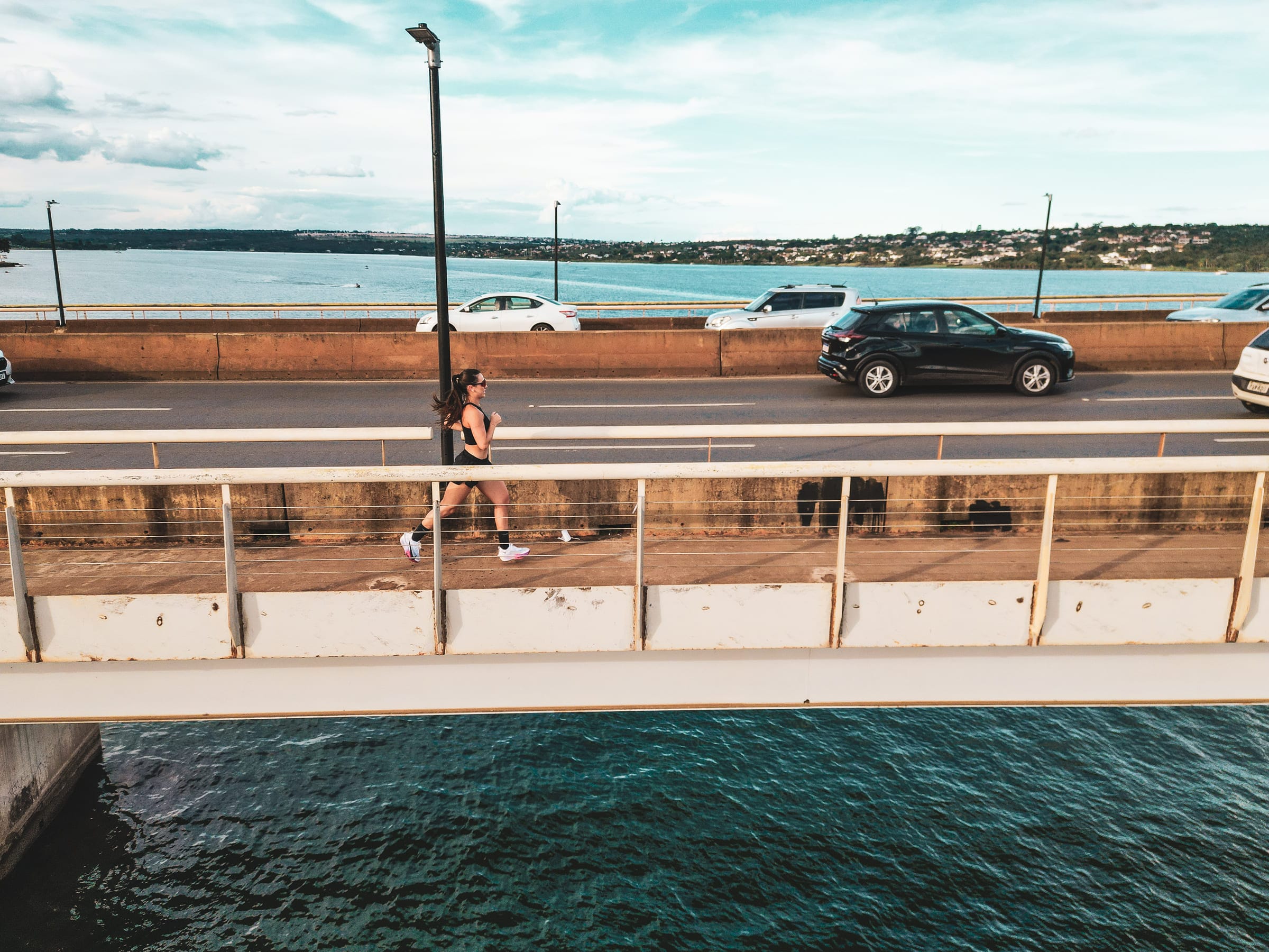 Vista aérea da ponte sobre o Lago Paranoá com Cristina correndo na passarela
