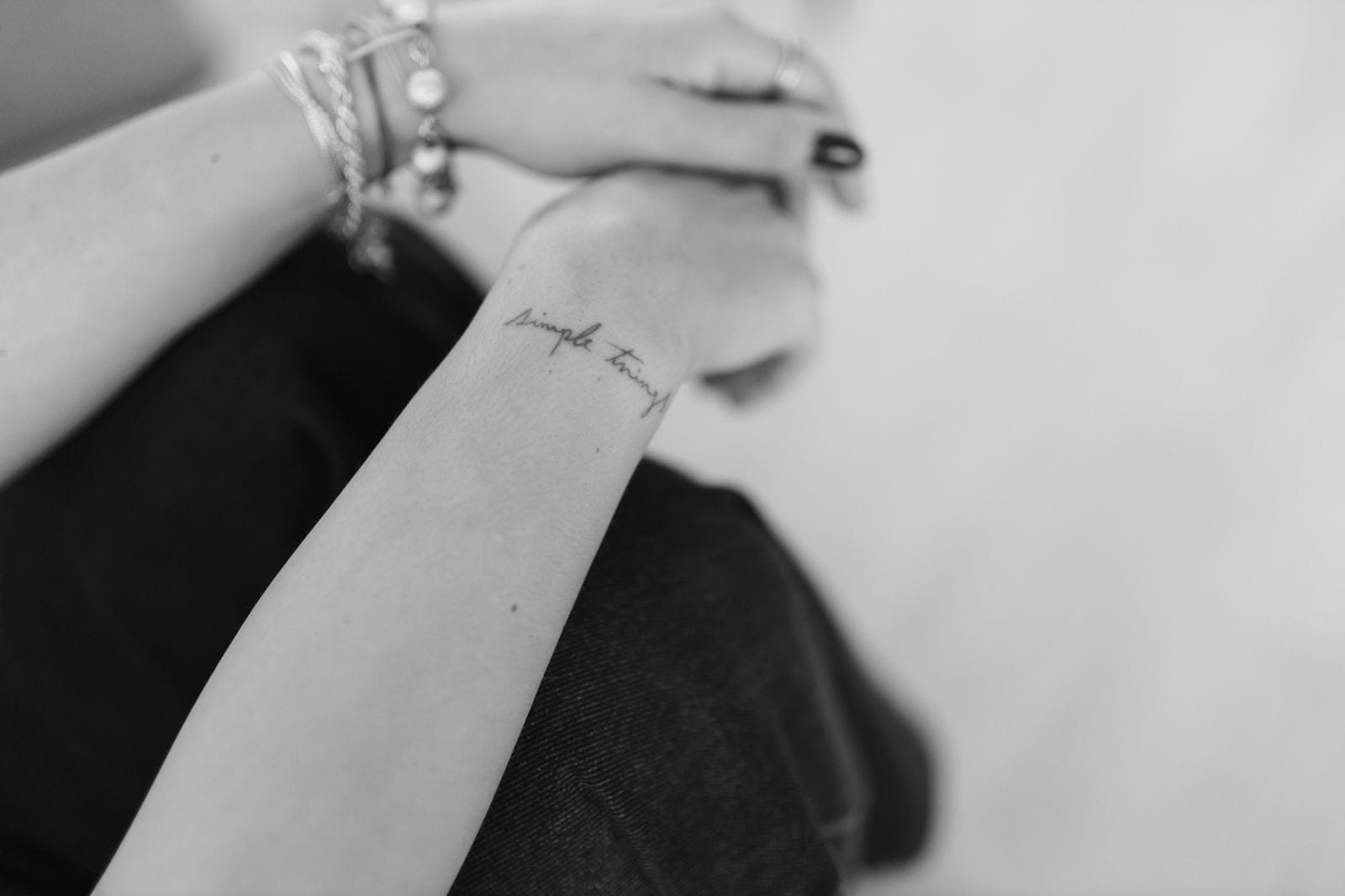 Detalhe em preto e branco das mãos de Cristina, com pulseiras e uma tatuagem escrita no antebraço