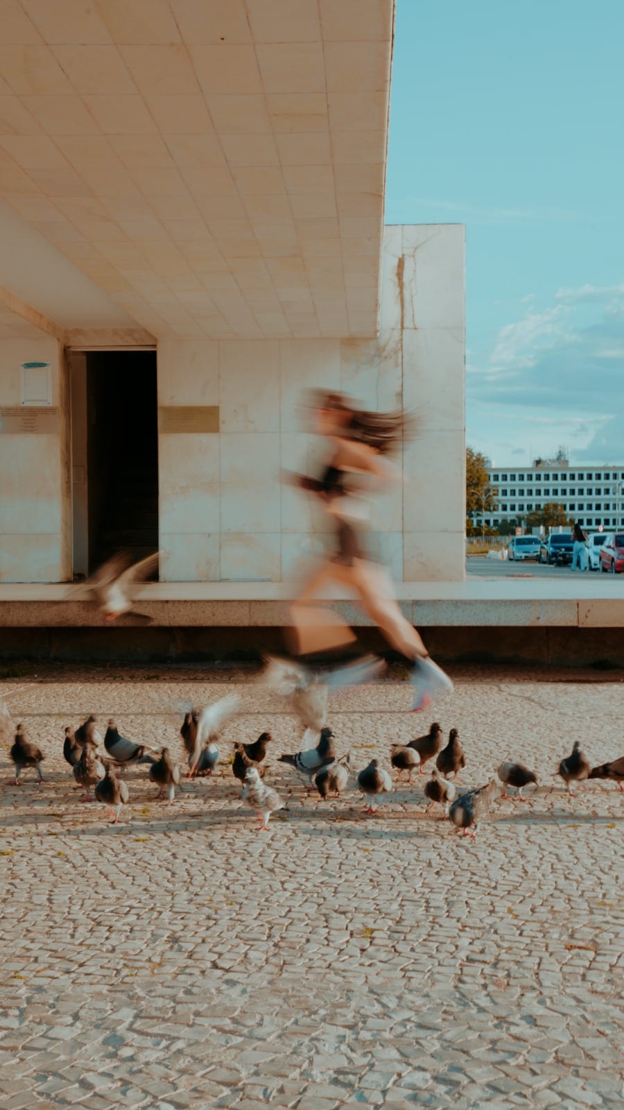 Cristina correndo diante da arquitetura modernista de Brasília enquanto pombos levantam voo