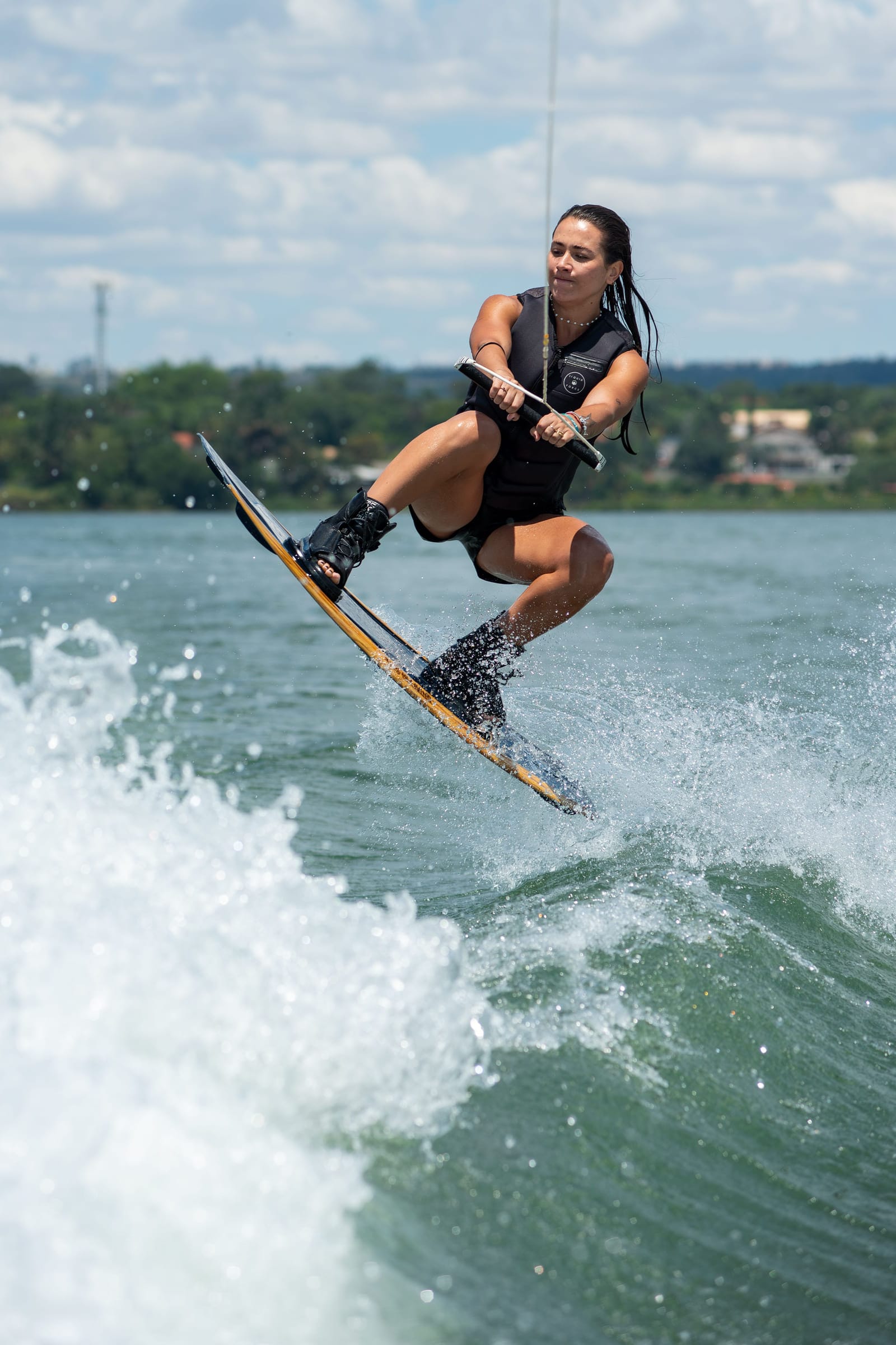 Cristina em salto de wakeboard, suspensa no ar acima da esteira de água