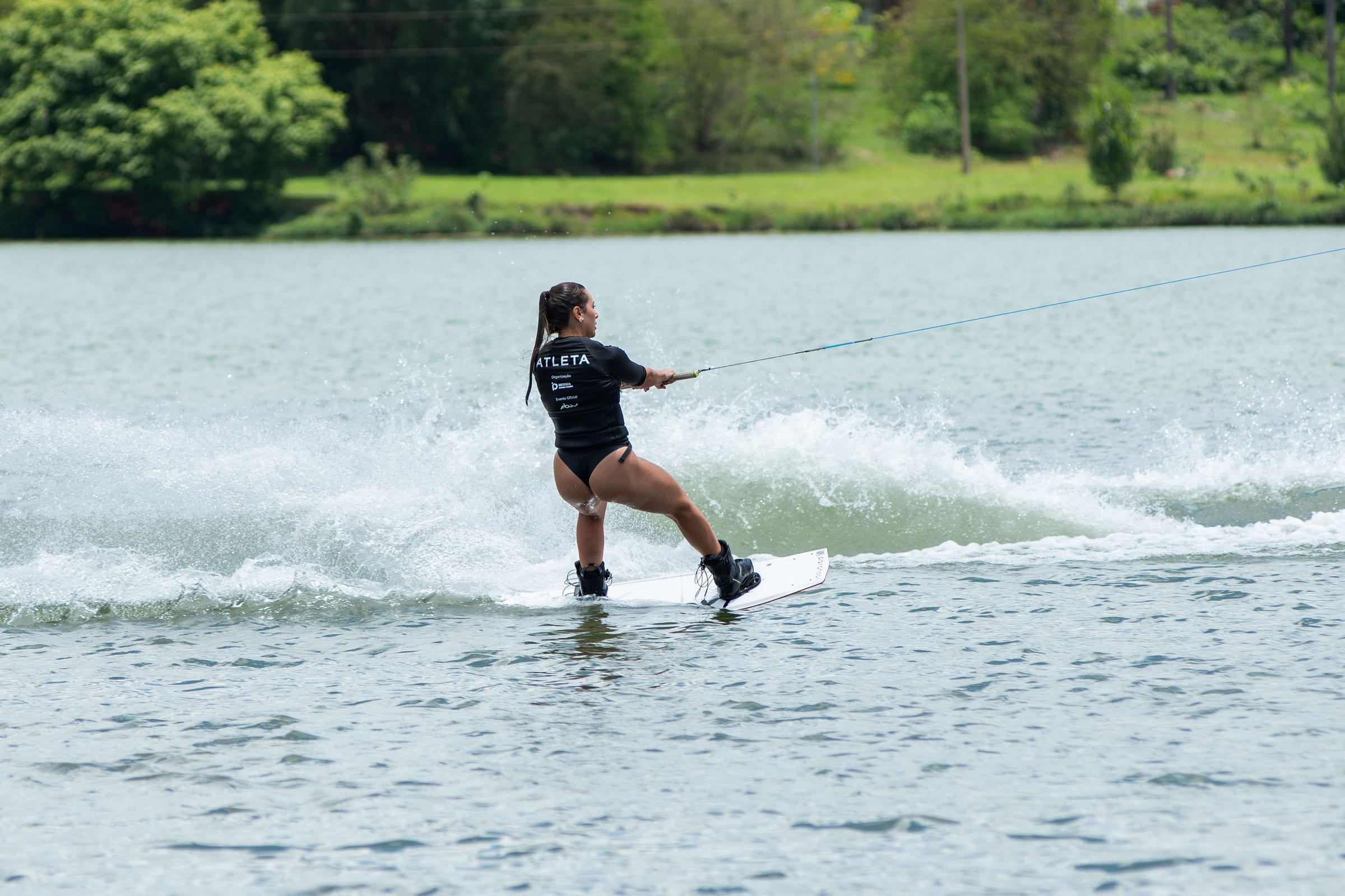 Cristina cortando a água de wakeboard, deixando um rastro branco atrás da prancha